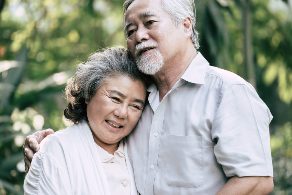 A senior man caring for his senior wife by embracing her with one arm