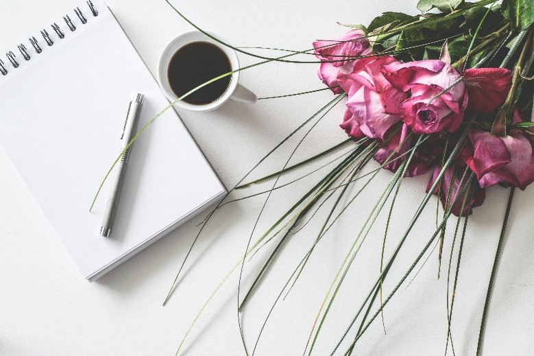 A bouquet of pink roses and a cup of coffee and a writing pad