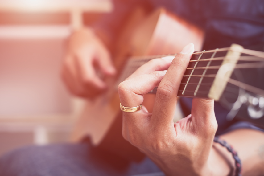 Woman holding a guitar with her left hand on the strings and her right hand strumming