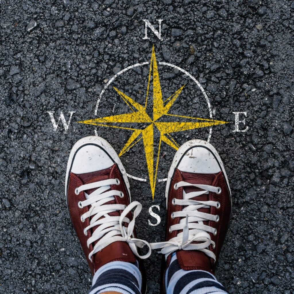 Red-clad running shoes on two feet standing on a compass pointing north
